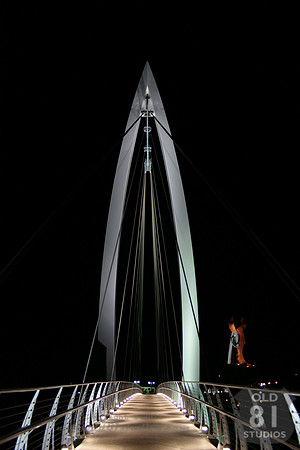 Color Photograph of the bow suspension bridge with The Keeper of the Plains in the background in Wichita Kansas.