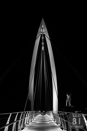 b/w (black and white) Photograph of the bow suspension bridge with The Keeper of the Plains in the background in Wichita Kansas.