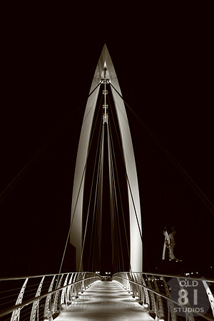 Sepia Photograph of the bow suspension bridge with The Keeper of the Plains in the background in Wichita Kansas.